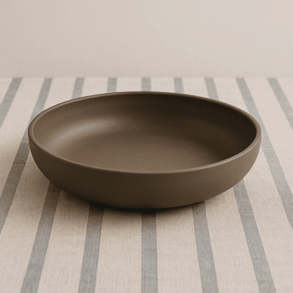 Κεραμικό πιάτο γαβάθα σε σκούρο πηλό πάνω σε ριγέ υφασμάτινη επιφάνεια.