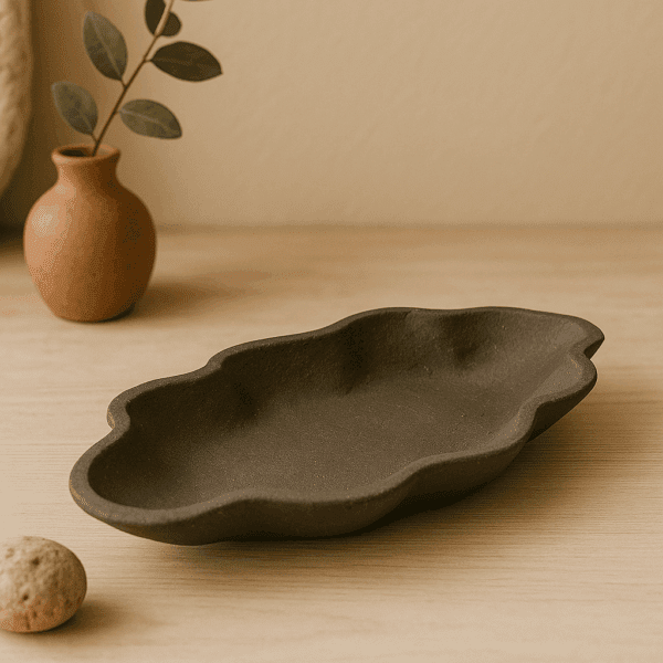 χειροποίητο κεραμικό πιάτο κοχύλι από μαύρο πηλό και μαύρο γυάλωμα σε φυσικό σκηνικό με φυτά, ξύλο και γήινους τόνους